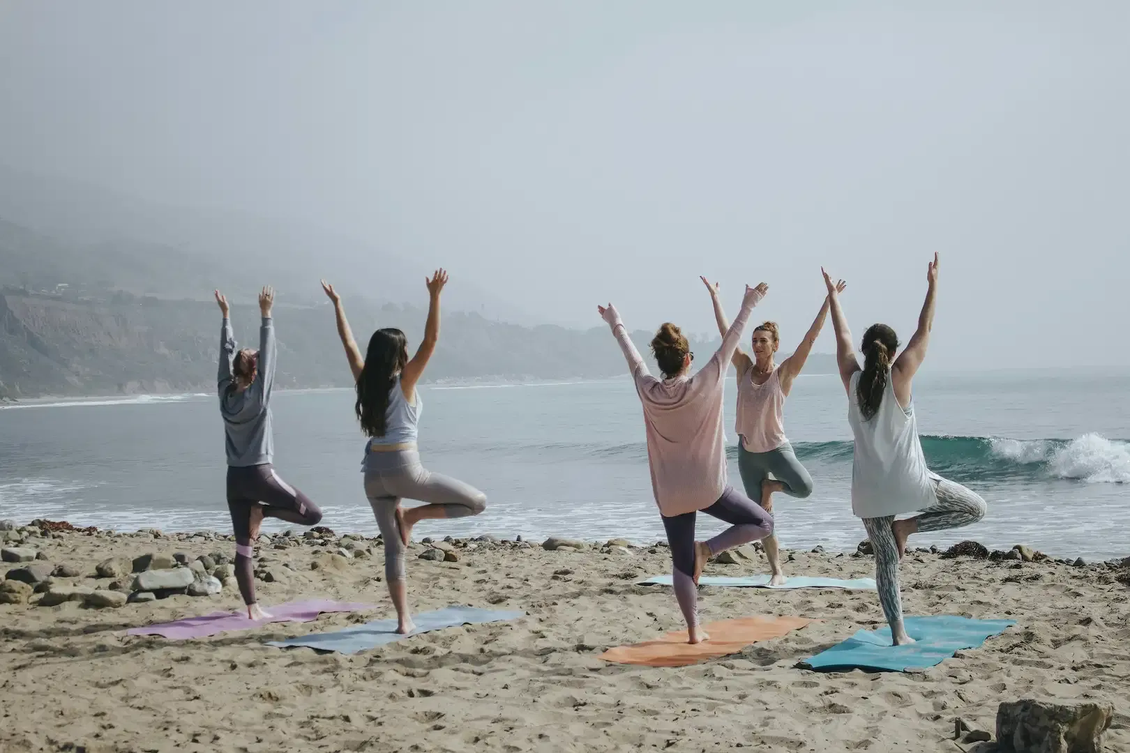 Group practicing tree pose yoga together on a beach