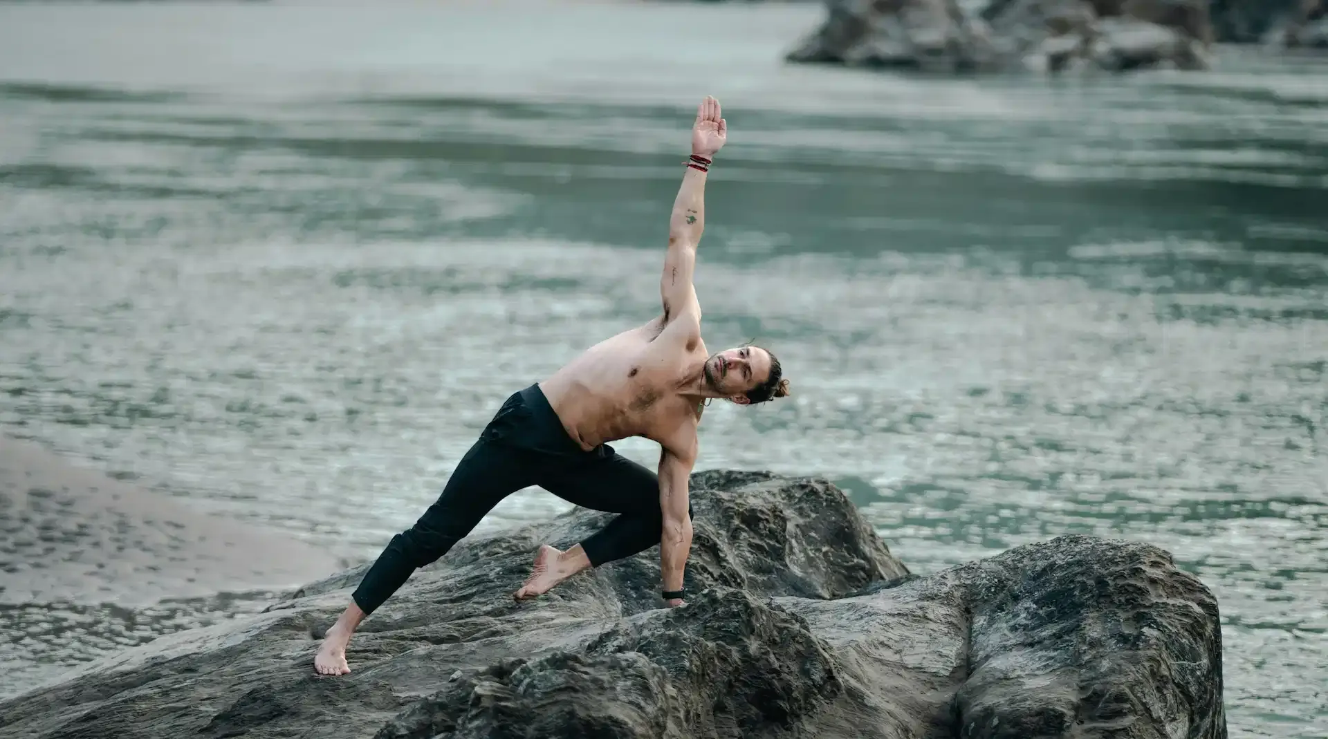 Man performing a yoga pose on rocks beside water