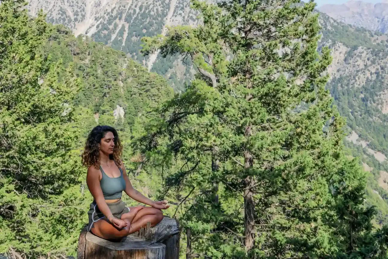 Woman meditating cross-legged on a tree stump in the mountains