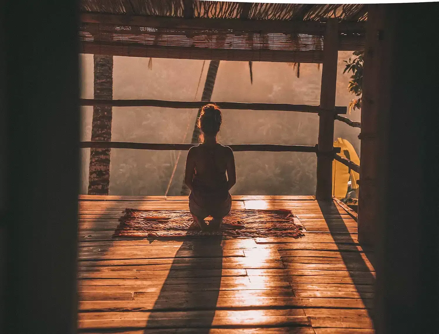Silhouette of a person kneeling in meditation on a wooden deck at sunset