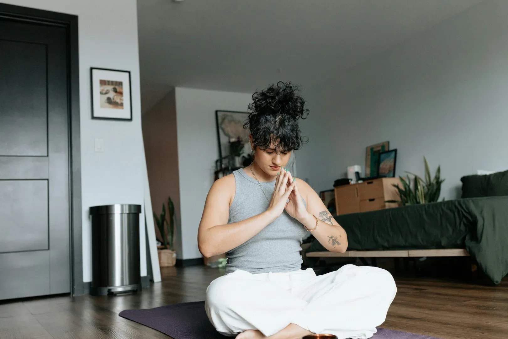 Woman sitting cross-legged in prayer position meditating indoors