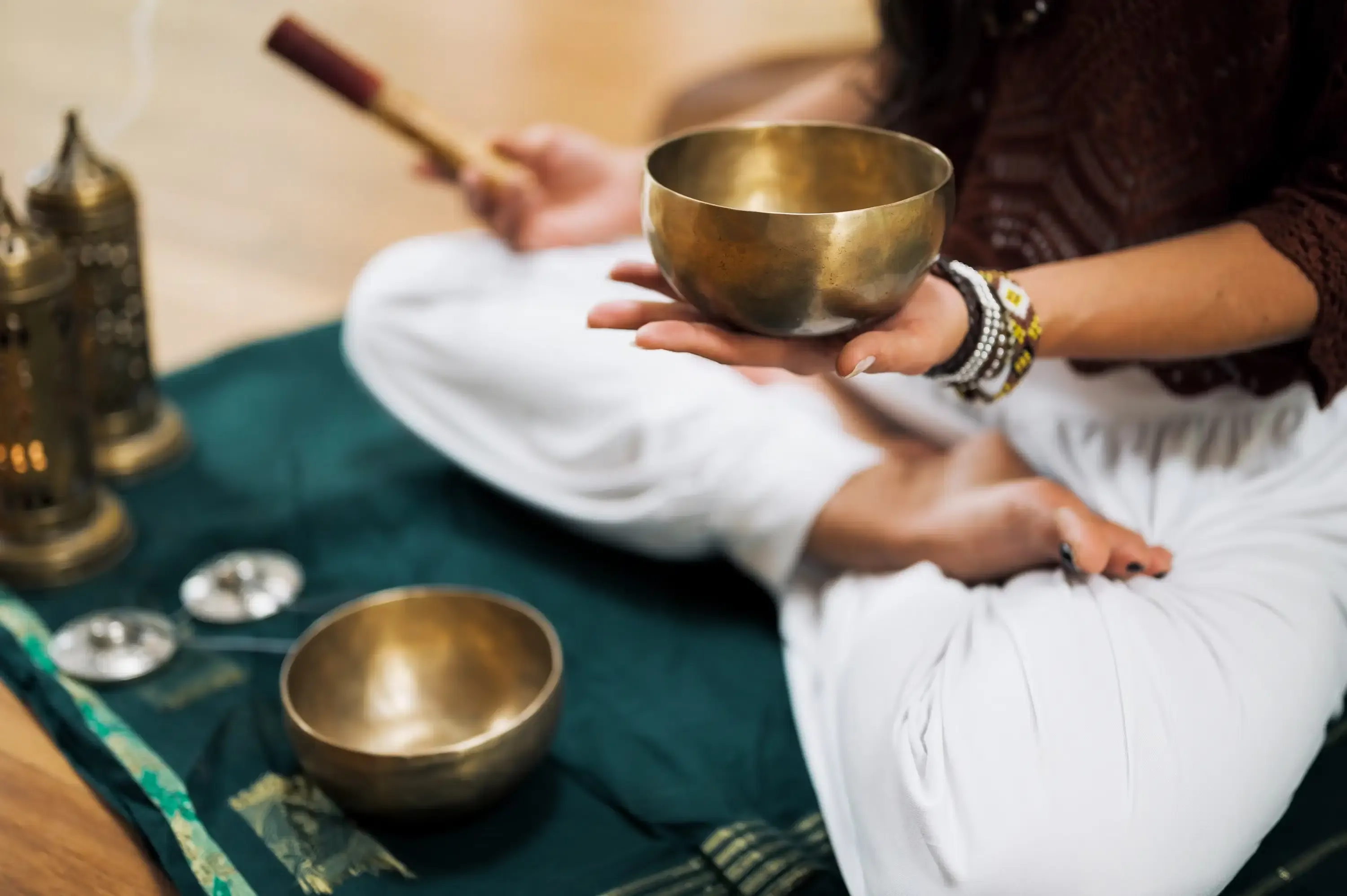 Hands holding a singing bowl with incense and cymbals nearby