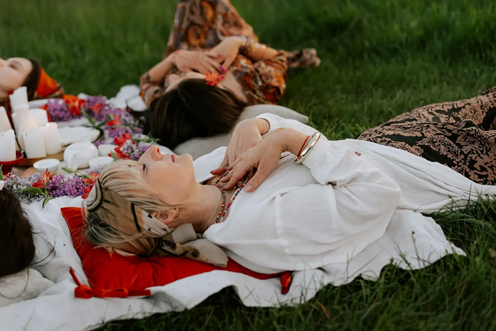 Women lying outdoors with eyes closed among flowers and candles