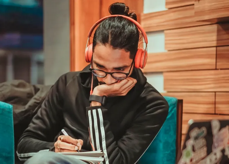 Man wearing red headphones writing notes while listening to music