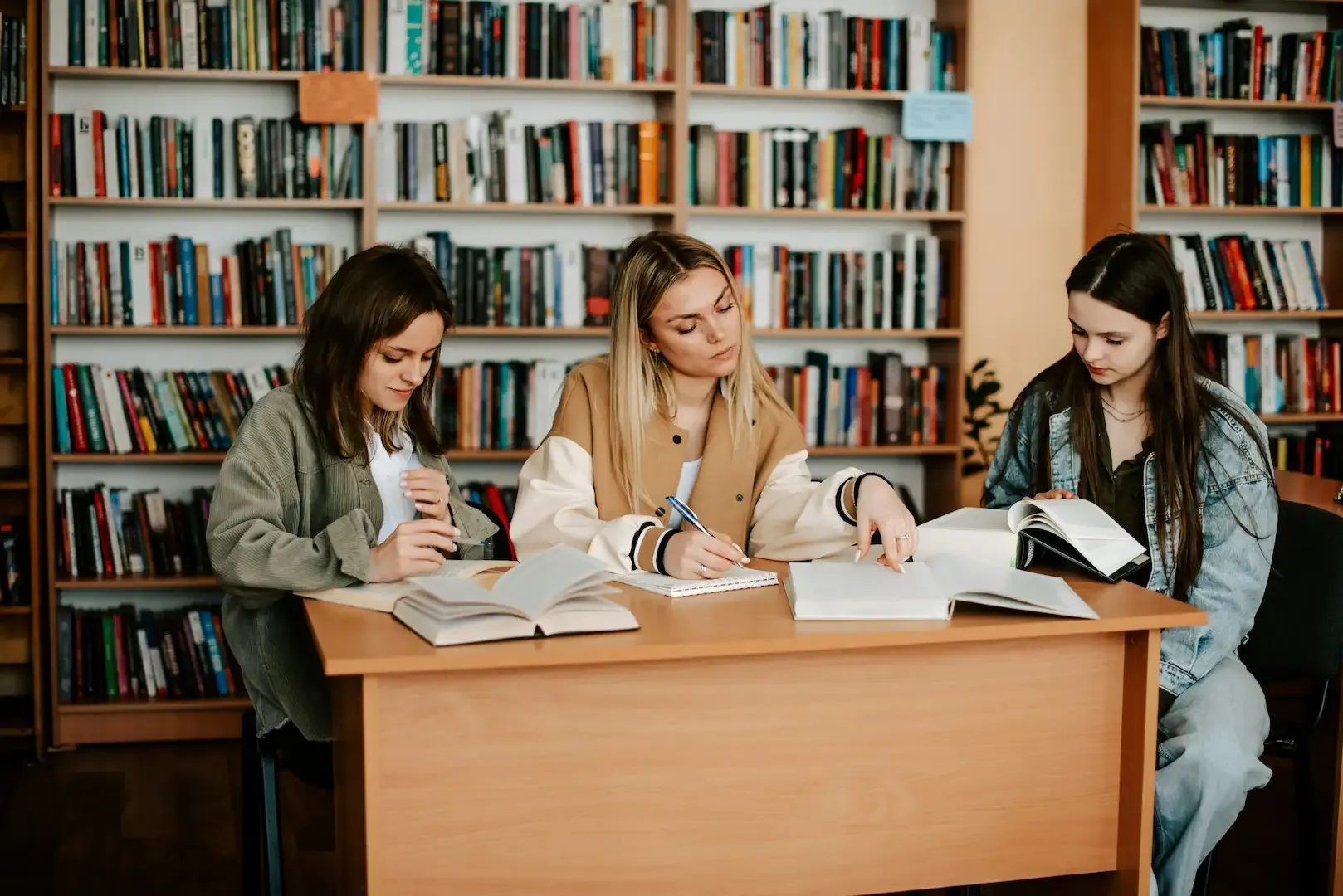 Three students studying together with books at a library table