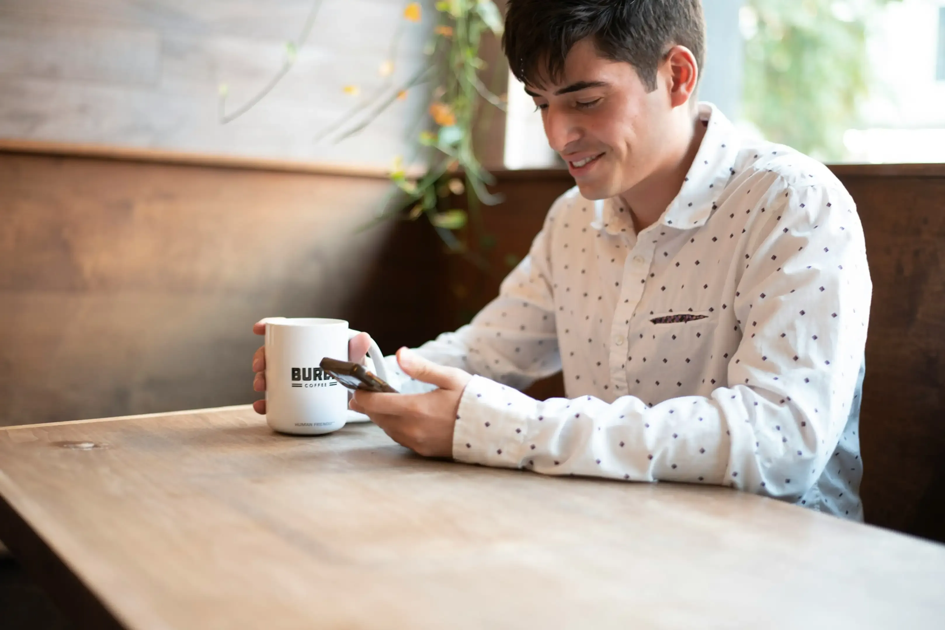 Smiling man checking his phone over coffee at a wooden table